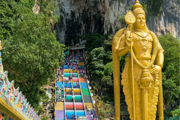 Gouden beeld van Lord Murugan naast de kleurrijke trappen van de Batu Caves