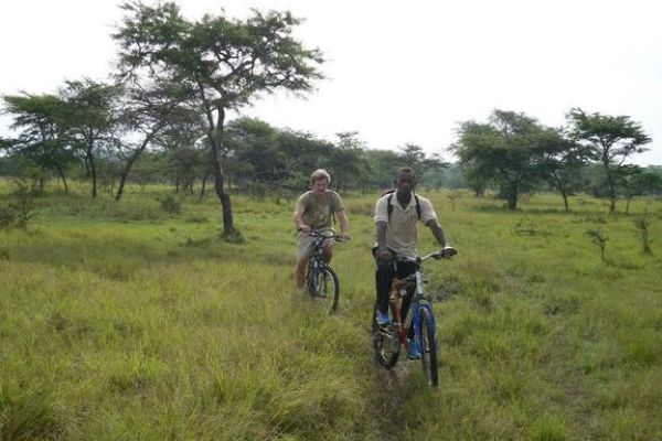 Ranger en reiziger op fietssafari in Lake Mburo National Park tussen zebrapaden en savanne