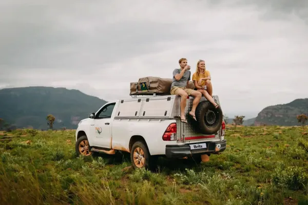 Witte Toyota Hilux Single Cab 4×4 met groene daktent en ladder, opgesteld in droog grasland met acaciaboom op de achtergrond.jpg