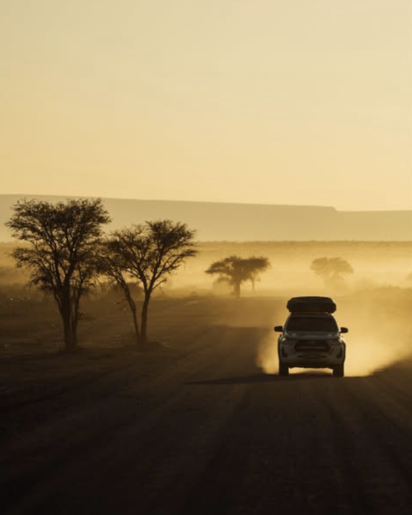 “4x4 auto rijdt over een verlaten gravelweg door het uitgestrekte landschap van Afrika tijdens een rondreis.”