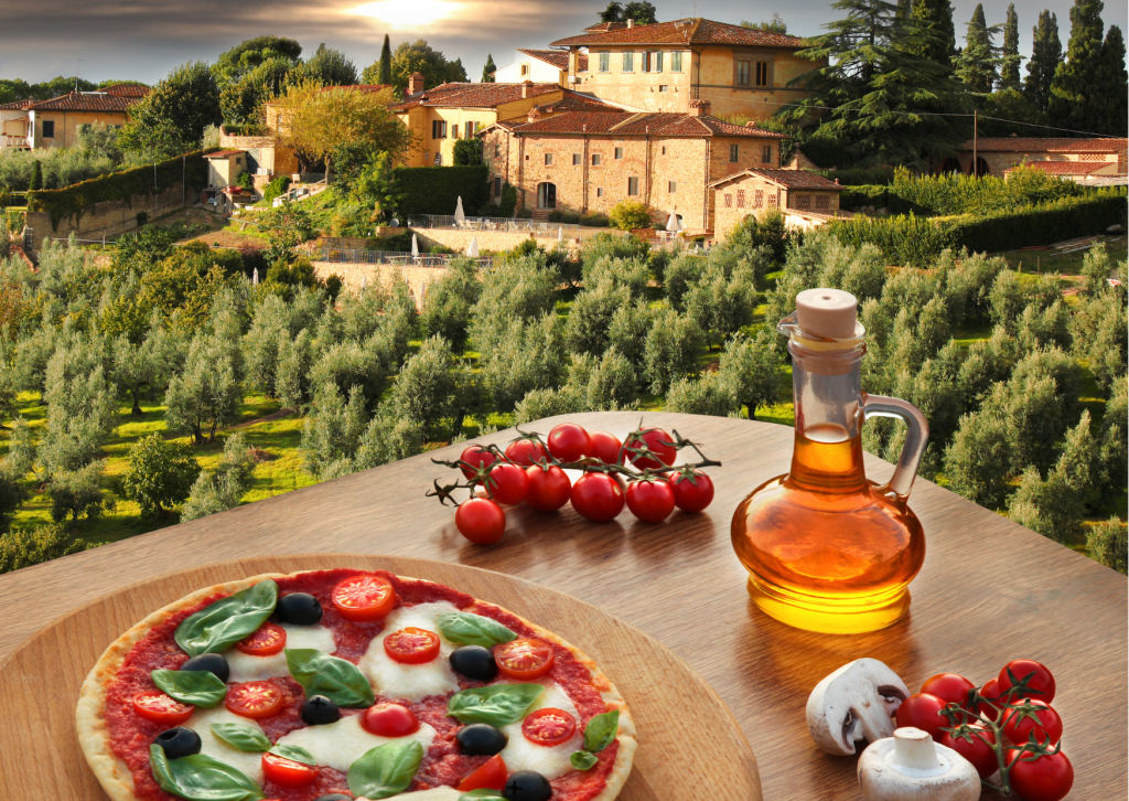 Italiaans eten met verse pasta, pizza en mediterrane ingrediënten op een tafel met uitzicht op een dorpje in Italië.